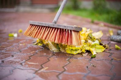 Close-up photograph of the bottom of a broom over a mountain of autumn leaves to be removed. It has recently rained and everything is wet