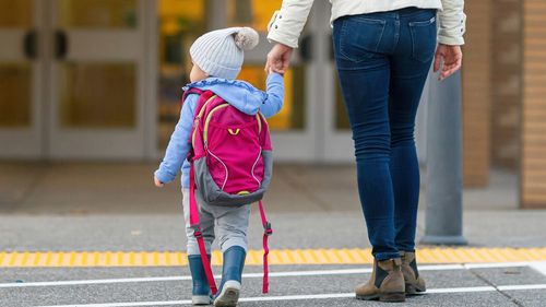 Vista posteriore di una giovane madre allegra che tiene la mano della figlia mentre cammina sulle strisce pedonali verso la scuola del bambino.