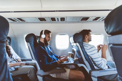 Young bearded man sitting inside an airplane and using a laptop. Male passenger using computer during flight.