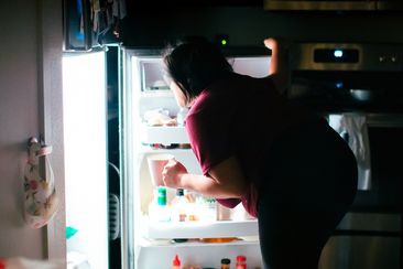 A pregnant woman is getting into the kitchen refrigerator at midnight to get a snack. Giving into her pregnancy cravings.