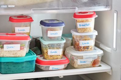 Plastic containers of food labeled for different meals stacked on a shelf inside of a refrigerator