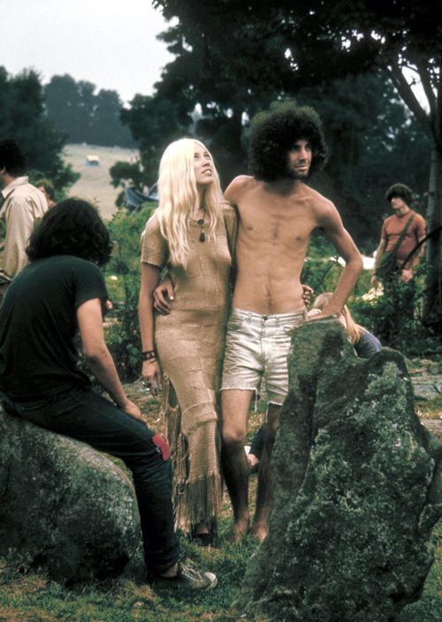 A hippie couple pose together arm in arm with others around them, during the Woodstock music festival in 1969.