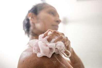 Woman applying soap with loofah while taking shower in bathroom.