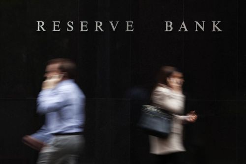 Due persone al telefono che camminano in direzioni opposte fuori dalla Reserve Bank of Australia, a Sydney. La foto è stata scattata con una sfocatura voluta.