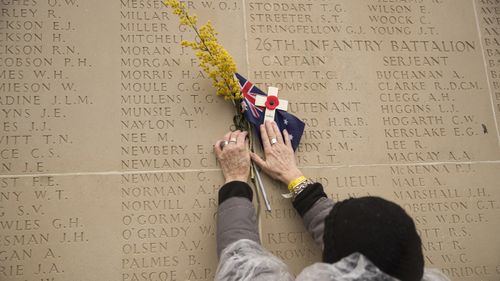 A woman holds up a small cross and an Australian flag to a wall bearing the names of the missing at the end of an Armistice ceremony at the World War I Australian National Memorial in Villers-Bretonneux, France, Sunday, Nov. 11, 2018.