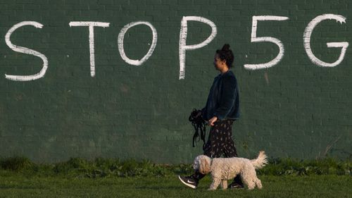 A woman in England walks past an anti-5G graffiti message.