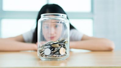 Woman staring through a jar filled halfway with coins.