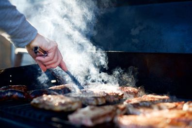 Turning with thongs, Steak and sausages on a barbecue with smoke.