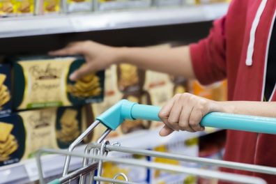 Woman using trolley cart while walking and taking products from shelf in a grocery store.