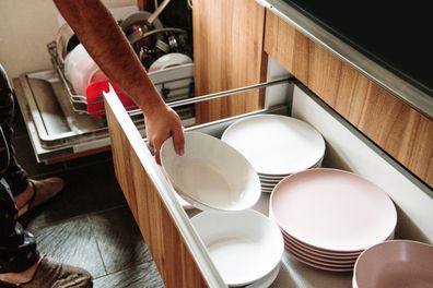 A man arranging in a drawer the dishes recently cleaned in the dishwasher