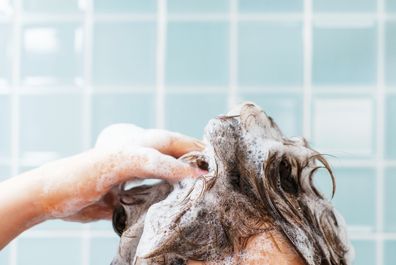 Female hands wash their hair with shampoo with foam on a blue background, front view.