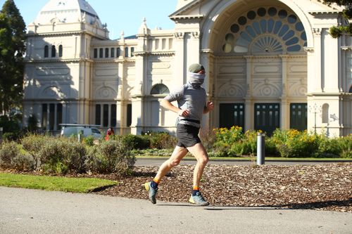 A man wearing a face cover runs through the Carlton Gardens in Melbourne, Australia