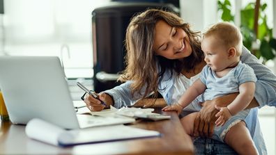 Work from home flexible work life working mum at desk holding baby juggling home work life balance