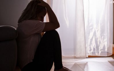 Sad woman sitting on floor of bedroom at home