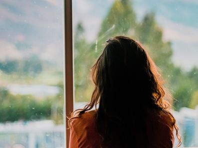 A woman looks out a window from behind. Stock photo.