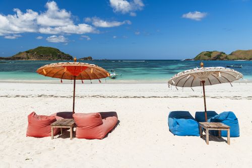 Ombrelloni colorati e sbuffi sulla spiaggia di sabbia bianca di fronte ad una laguna idilliaca, isola di Lombok, Indonesia