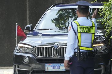 A security guard signals to a car with diplomatic plates and Chinese flag as he parks at the Philippine Department of Foreign Affairs in Manila, Philippines on Aug. 7, 2023.