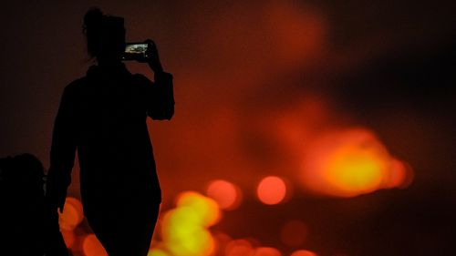 A woman records with her phone as lava erupts from the Mauna Loa volcano Thursday, December 1, 2022, near Hilo, Hawaii. 