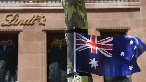 A flag blows in the wind, bearing the names of siege victims Tori Johnson and Katrina Dawson. (AAP)