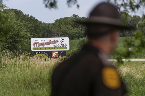 An Iowa State Patrolman walks past a Maquoketa Caves State Park sign as police investigate a shooting that left several people dead, Friday, July 22, 2022, in Maquoketa, Iowa. 