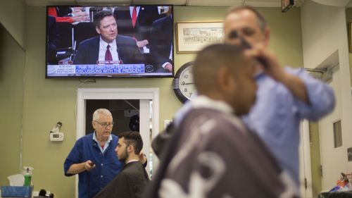 Barbers at Puglisi Hair Cuts in Washington tend to customers as televised coverage of former FBI director James Comey testifying plays out on June 8, 2017. Photo: AP