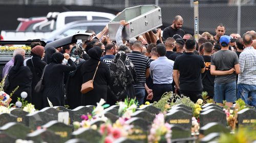 Mourners lift an empty coffin above their heads during the burial of Mick Hawi at Rockwood Cemetery. (AAP)