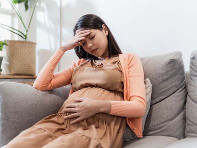 Pregnant woman sitting on couch with hand to head.