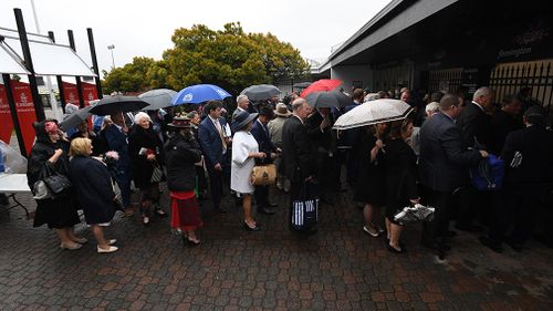 Racegoers line up in the rain outside Flemington Racecourse. (AAP)