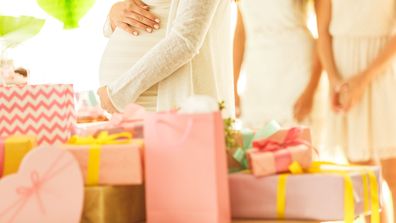 Mid section of pregnant woman holding her belly while standing by the table with a ppile of presents. Friends standing in the background.