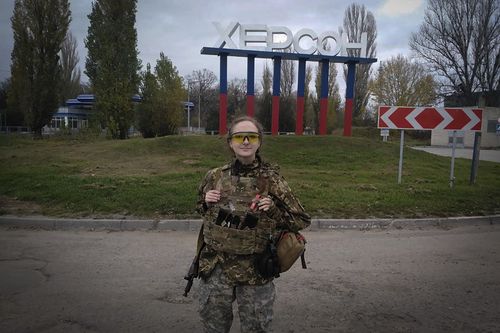 A Ukrainian female soldier poses for a photo against a Kherson sign in the background, in Kherson, Ukraine, Friday, November 11, 2022 