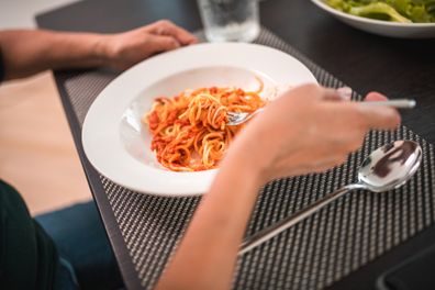 Elevated view on hands of a mature Hispanic female eating spaghetti at family lunch at home. Sitting at a table in a domestic dining room spending time with family.