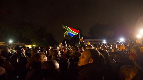 A South African flag soars through the darkness as mourners chant and sing in memory of Nelson Mandela's extraordinary life. (Getty)