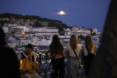 People watch a supermoon rise above Lisbon, Wednesday, Aug. 30, 2023.  