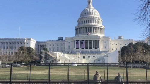 Members of the National Guard stand inside anti-scaling fencing that surrounds the Capitol, Sunday, Jan. 10, 2021, in Washington. The inaugural stand is centre