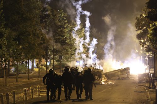 Riot police officers patrol as smoke billows from burnt vehicles on the third night of protests sparked by the fatal police shooting of a 17-year-old driver in the Paris suburb of Nanterre, France, Friday, June 30, 2023. 