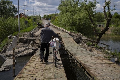 A man pushes his bicycle across a repaired bridge in Vilkhivka, outside Kharkiv, in eastern Ukraine, Friday, May 20, 2022. (AP Photo/Bernat Armangue)