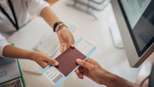 Two people, man in modern travel agency talking with woman who is working there, she is giving him a airplane ticket.