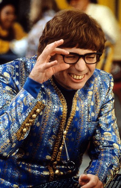 Mike Myers wearing an ornate blue jacket while squinting through his black rimmed glasses in a scene from the film 'Austin Powers: The Spy Who Shagged Me', 1999.