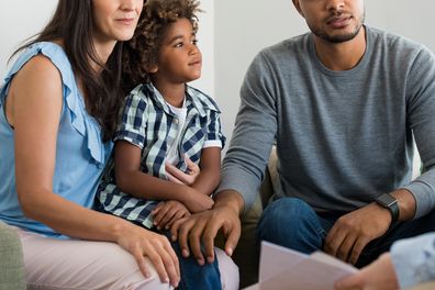 Serious couple with son in a deep conversation with family counselor. Multiethnic parents talking about adoption with their counselor. Family at the financial planning consultation.