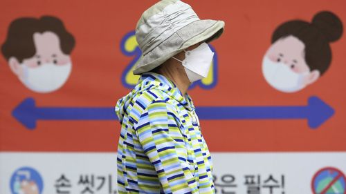 A woman wearing a face mask to help protect against the spread of the new coronavirus passes by a banner about precautions against the virus at a park in Goyang, South Korea, Tuesday, June 2, 2020