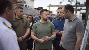 In this photo provided by the Ukrainian Presidential Press Office, Ukrainian President Volodymyr Zelenskyy, center, surrounded by ambassadors of different countries and UN officials, visits a port in Chornomork during loading of grain on a Turkish ship, background, close to Odesa, Ukraine, Friday, July 29, 2022. (Ukrainian Presidential Press Office via AP)