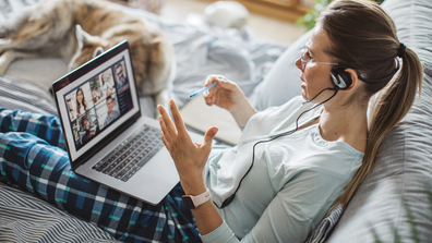 Woman sits in bed in what appears to be a work meeting 