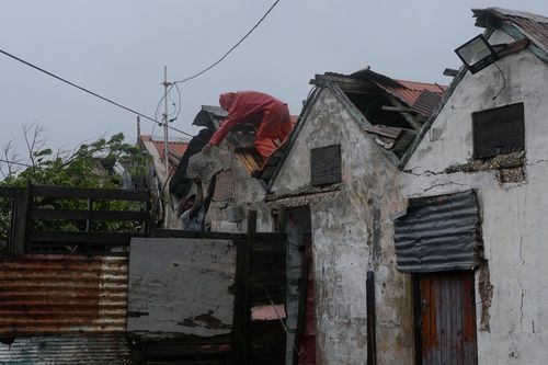 Homens removem uma seção solta do telhado em Kingston, Jamaica, enquanto o furacão Melissa se aproxima, terça-feira, 28 de outubro de 2025. (AP Photo/Matias Delacroix)