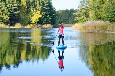 Active woman paddling SUP board on beautiful lake, autumn forest landscape and nature on background, stand up paddling water adventure outdoors, sport and healthy lifestyle concept