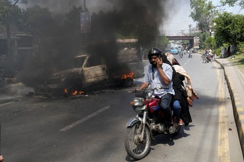 یک موتورسوار از کنار خودرویی در حال سوختن می گذرد که توسط حامیان خشمگین عمران خان نخست وزیر سابق پاکستان در لاهور پاکستان به آتش کشیده شده است، پنجشنبه 11 می 2023.  