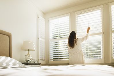 woman opening blinds in bedroom