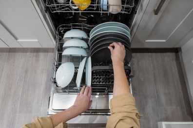 A point of view shot of an unrecognisable mature caucasian woman emptying a dishwasher full of clean crockery in her kitchen at home.