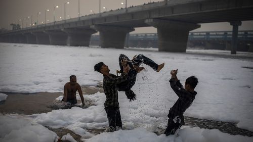 Young Hindu devotees play in Yamuna river, covered by chemical foam caused due to industrial and domestic pollution, during Chhath Puja festival in New Delhi, India, Wednesday, Nov. 10, 2021. A vast stretch of one of India's most sacred rivers, the Yamuna, is covered with toxic foam, caused partly by high pollutants discharged from industries ringing the capital New Delhi. Still, hundreds of Hindu devotees Wednesday stood knee-deep in its frothy, toxic waters, sometimes even immersing themselves
