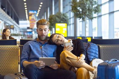 Young woman and man traveling by plane, using a digital tablet and smart phone in airport departure area.