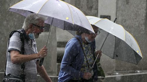 Pedestrians use umbrellas to shield the rain in Sydney, Wednesday, March 2, 2022, as parts of Australia's southeast coast were inundated by the worst flooding in more than a decade. Floodwaters are moving south into New 